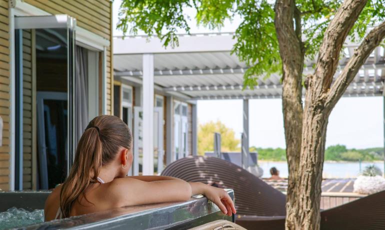 Relaxed woman in outdoor hot tub, view of green garden.