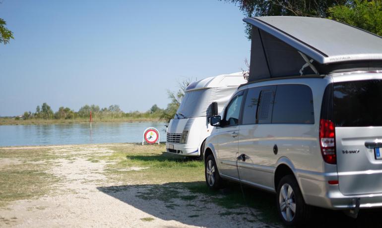 Campers parked near a lake with a prohibition sign.