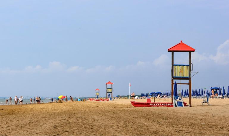 Sandy beach with lifeguard towers and blue umbrellas, people in the distance.