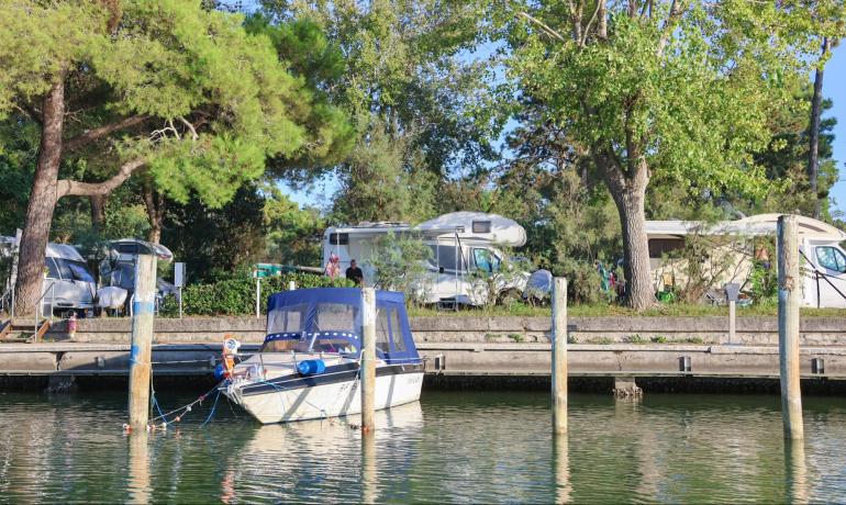 Campers and boat by the lake, surrounded by trees.