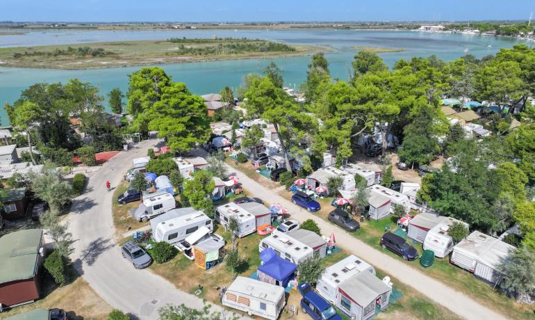 Camping site with caravans near a river and green trees.