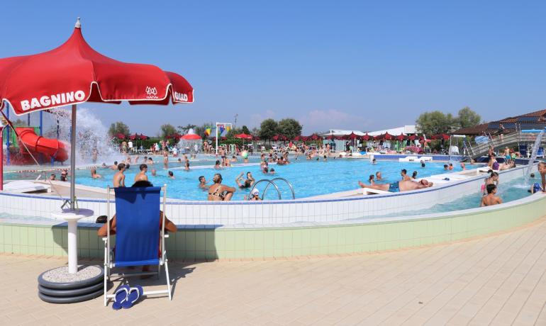 Crowded pool with lifeguard, slide, and red umbrellas.