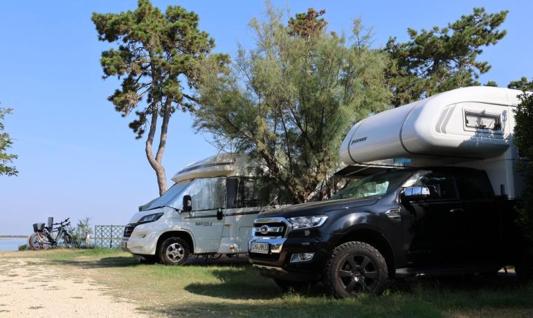 Campers parked near the lake under green trees and blue sky.